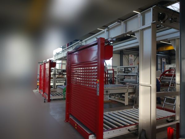 Industrielle Behälterstation mit roten vertikalen Trennwänden und Förderrollen in einer Halle