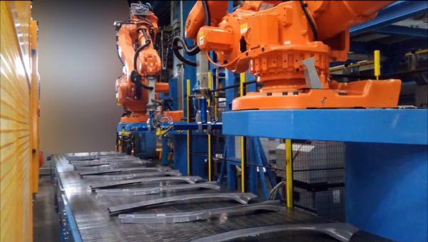 Blick entlang eines automatischen Stapelsystems. Mehrere Presshärtebauteile liegen auf dem Auslaufband, während Roboter für die automatische Entnahme und Stapelung bereitstehen.