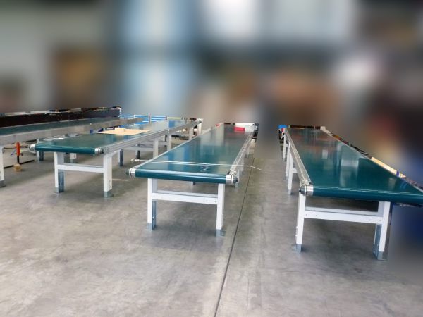 Drei grüne Auslaufbänder mit weißen Metallgestellen in einer großen Halle mit Betonboden