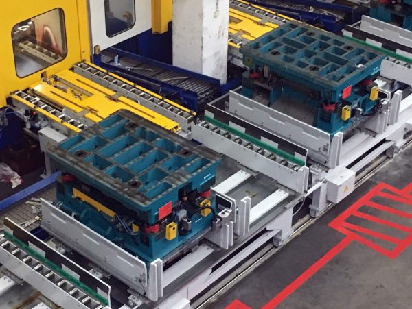 Werkzeugwechselvorrichtung mit mehreren blauen Werkzeughaltern auf weißen Schienen in einer Industriehalle