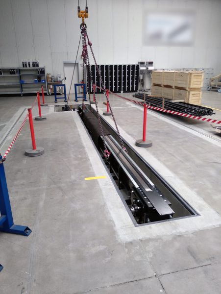 Gesamtansicht eines Taktantriebs während der Installation in einer Bodengrube. Die Antriebseinheit wird mit einem Hallenkran in die vorbereitete Einbaustelle abgesenkt.