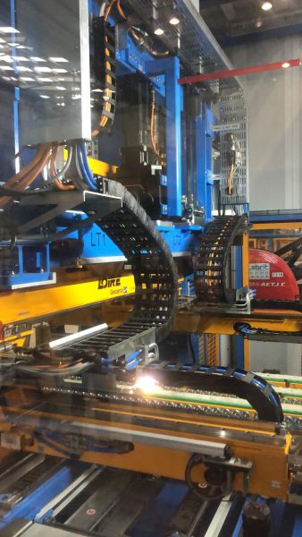 Industrielle Transfersysteme mit flexiblen Kabelketten und blauen sowie gelben Metallrahmen in einer Fertigungshalle