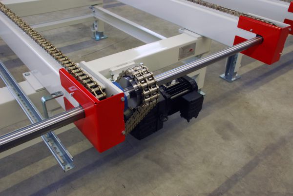 Nahaufnahme eines Kettenförderers mit zwei parallelen Ketten, roten Halterungen und einem schwarzen Elektromotor auf grauem Boden