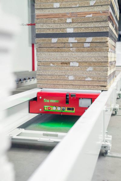 Schrägansicht eines LineMover-Shuttles unter einem Plattenstapel. Das Fahrzeug befindet sich auf der Führungsschiene und trägt den Materialstapel innerhalb der Förderstrecke.