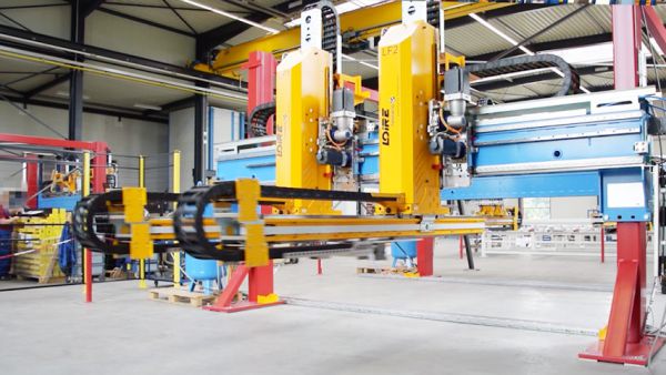 Industrielle Transfersystemanlage mit blauer Rahmenkonstruktion, gelben Greifern und Steuerungseinheiten in einer Werkhalle.