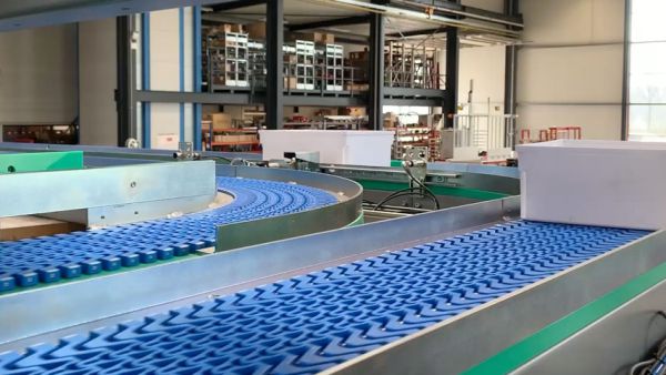 An apron conveyor with a blue conveyor belt and a green frame in an industrial building 