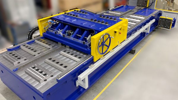 Blue and yellow horizontal press with a roller conveyor and safety guard in a factory building