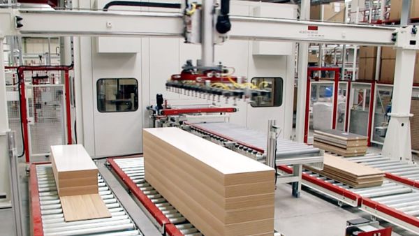 Portal-Feedersystem mit rotem Greifarm und gelben Schläuchen über einem Förderband mit gestapelten Holzplatten in einer Industriehalle