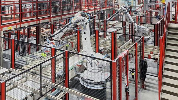 Gesamtansicht einer automatisierten Beschick- und Abstapellinie mit mehreren Robotern, Förderstrecken und Materialhandling-Systemen innerhalb einer Fertigungshalle.