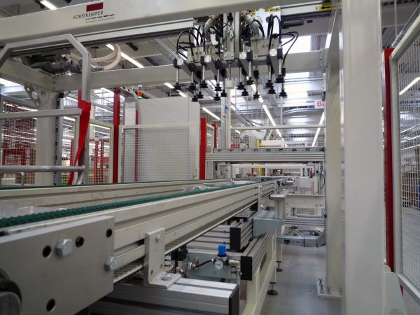 Riemenförderer in einer industriellen Fertigungshalle mit mehreren Greifarmen und Schutzgittern