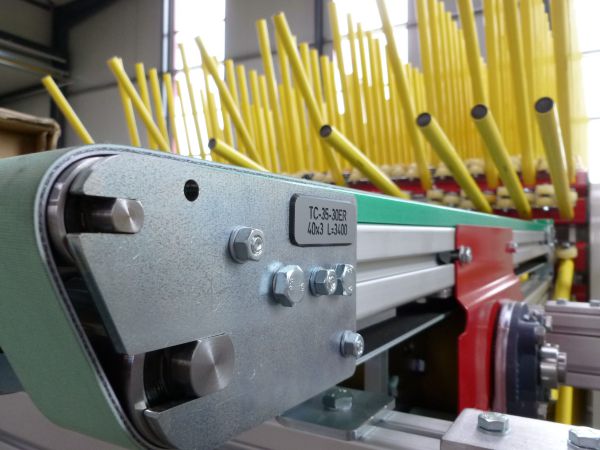 Detailansicht der Fördertechnik eines Igelpuffers. Im Vordergrund sind Förderband und Umlenkrolle zu sehen, im Hintergrund die dicht angeordneten Aufnahmestäbe des Speichers.