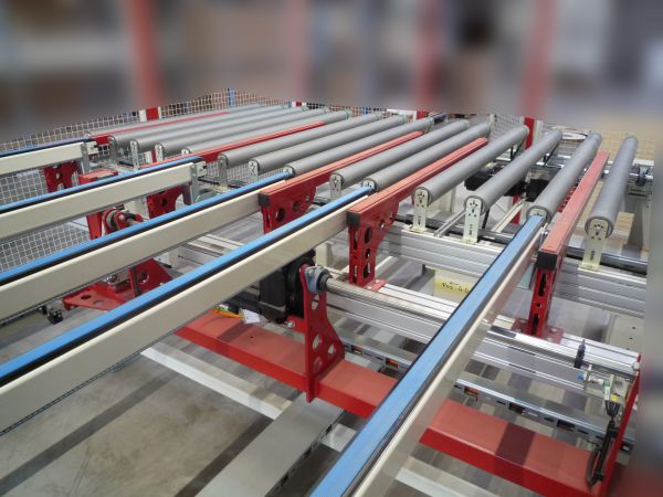 Förderanlage mit mehreren parallelen, silbernen Rollenbahnen und roten Stützrahmen in einer Industriehalle