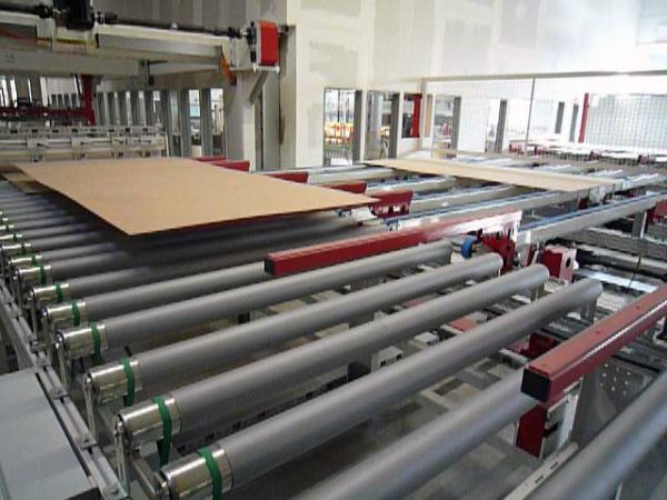 Industrielle Beschickungsanlage mit mehreren parallel angeordneten Rollenförderern und einem Hubrechen für den 90°-Winkel-Produkttransport in einer Halle