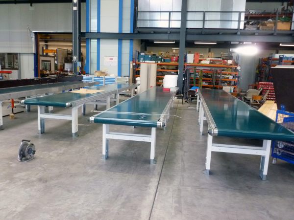 Gurtbandförderer mit länglichen grünen Förderbändern in einer Industrieumgebung auf Metallgestellen.