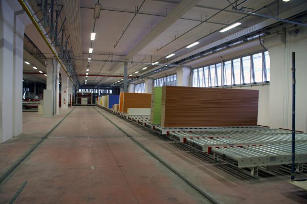 Rollenförderer in einer Lagerhalle mit gestapelten Platten in verschiedenen Farben und großem Raum.