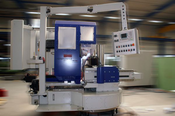 CNC-Bohrmaschine mit blauem Gehäuse, Steuerpult an einem Ausleger und mehreren Bedienknöpfen in einer Werkhalle
