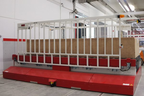 Seitenansicht eines Querförderwagens mit transportiertem Materialstapel. Das schienengeführte FTS bewegt die Last automatisiert zwischen den Lager- und Produktionsbereichen.