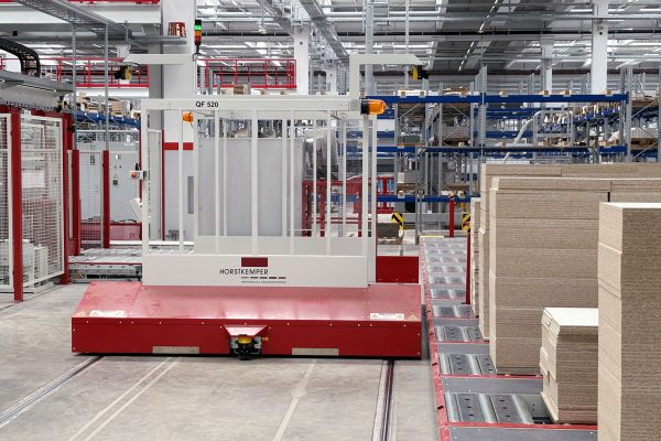 Frontansicht eines Querförderwagens an einer Materialübergabestation. Das FTS ist für die Aufnahme oder Übergabe von Materialstapeln positioniert.