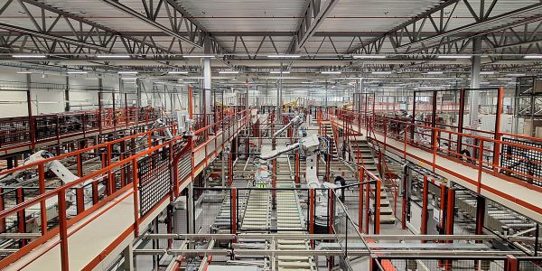 Gesamtansicht einer automatisierten Beschick- und Abstapellinie mit mehreren Robotern, Förderstrecken und Materialhandling-Systemen innerhalb einer Fertigungshalle.