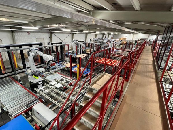 Gesamtansicht einer automatisierten Beschick- und Abstapellinie mit mehreren Robotern, Förderstrecken und Materialhandling-Systemen innerhalb einer Fertigungshalle.