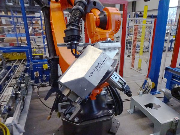 Detailansicht eines Industrieroboters mit montiertem Saug- und Greifsystem. Der Greifkopf ist angewinkelt positioniert und für die Aufnahme eines Werkstücks ausgerichtet.