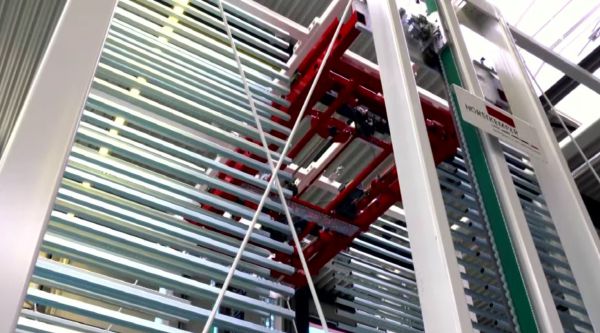 Detailansicht der Hub- und Transporteinheit eines Sortierspeichers. Die rote Transporteinheit ist zwischen den Speicherfächern verfahren und auf Höhe eines Lagerplatzes positioniert.