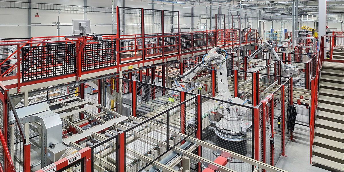 Overall view of an automated feeding and stacking line with multiple robots, conveyor lines, and material-handling systems within a production hall.
