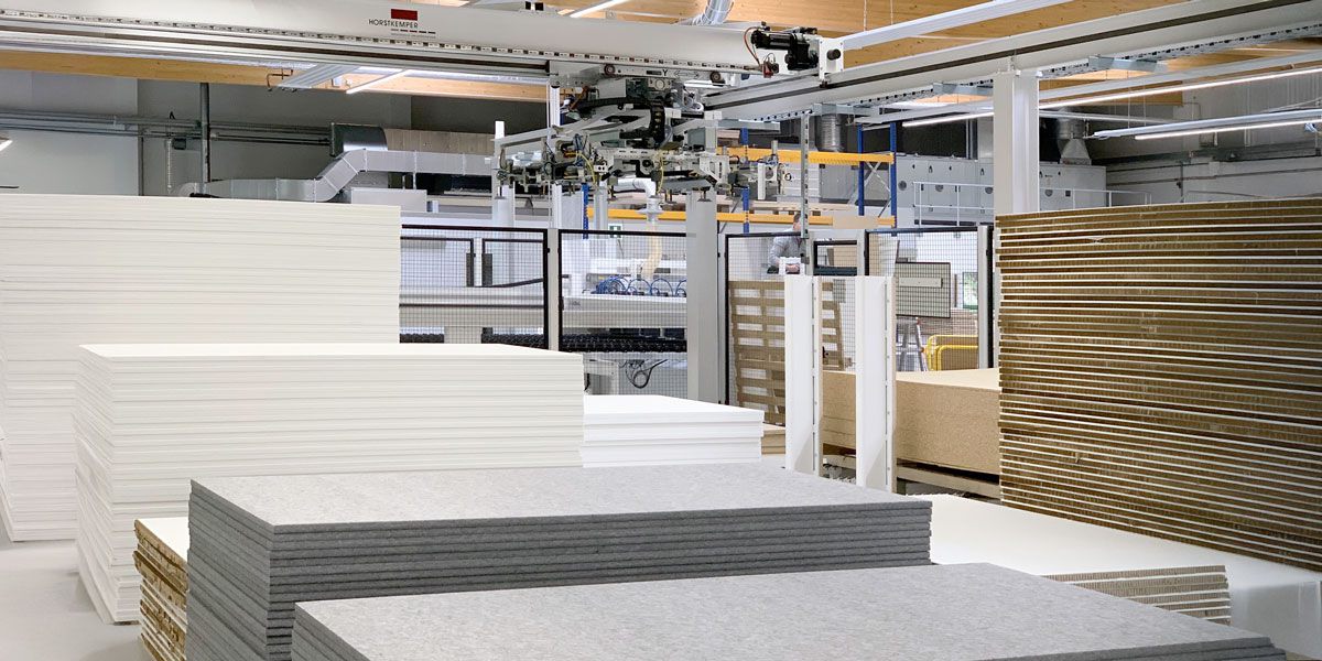 Overall view of an on-floor storage with several stacks of panels made of different materials. A gantry handling system for automated material retrieval is located above the storage areas.