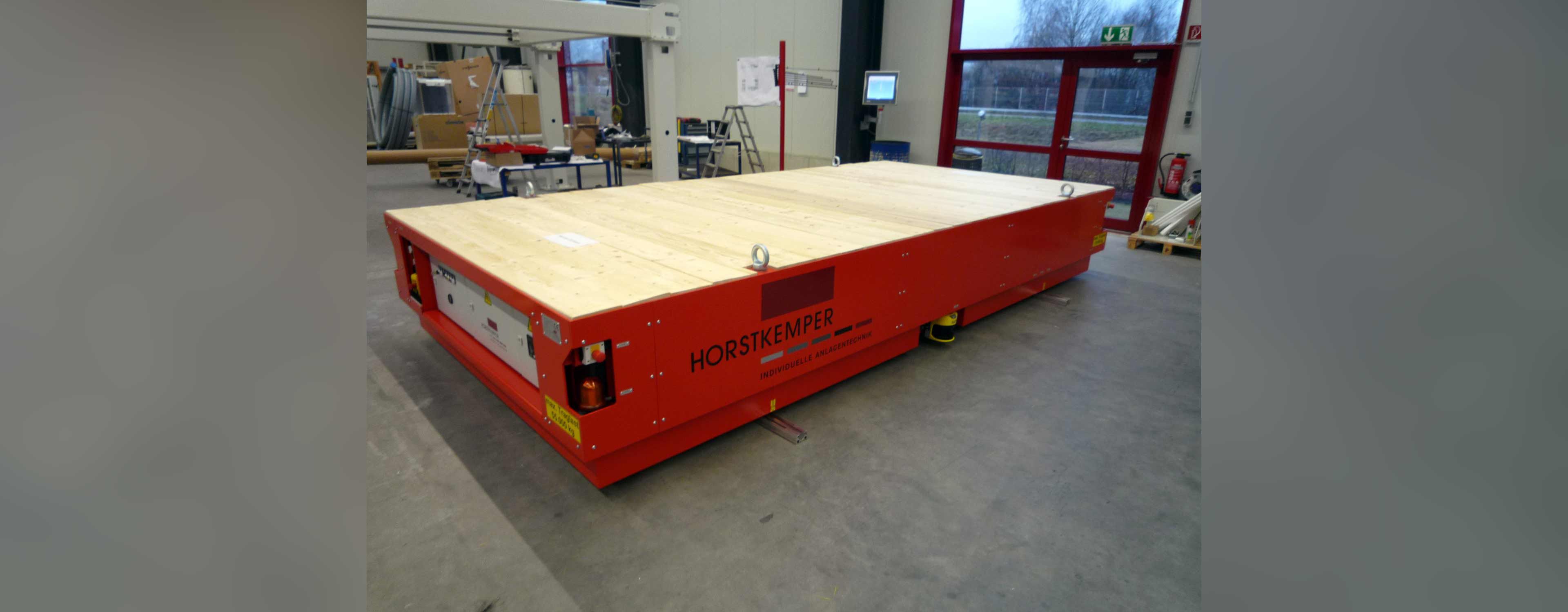 Sturdy industrial vehicle in bright red with a wooden transport surface and safety lights