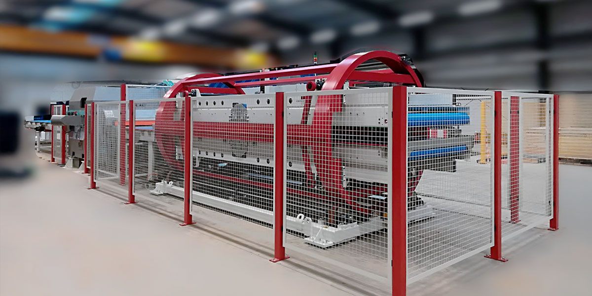 An angled view of a drum turner with a red rotating frame, a safety fence, and panels inserted in the transfer area.